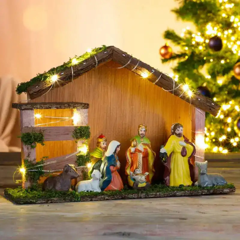 Illuminated wooden nativity scene with figurines in a stable-style shelter.